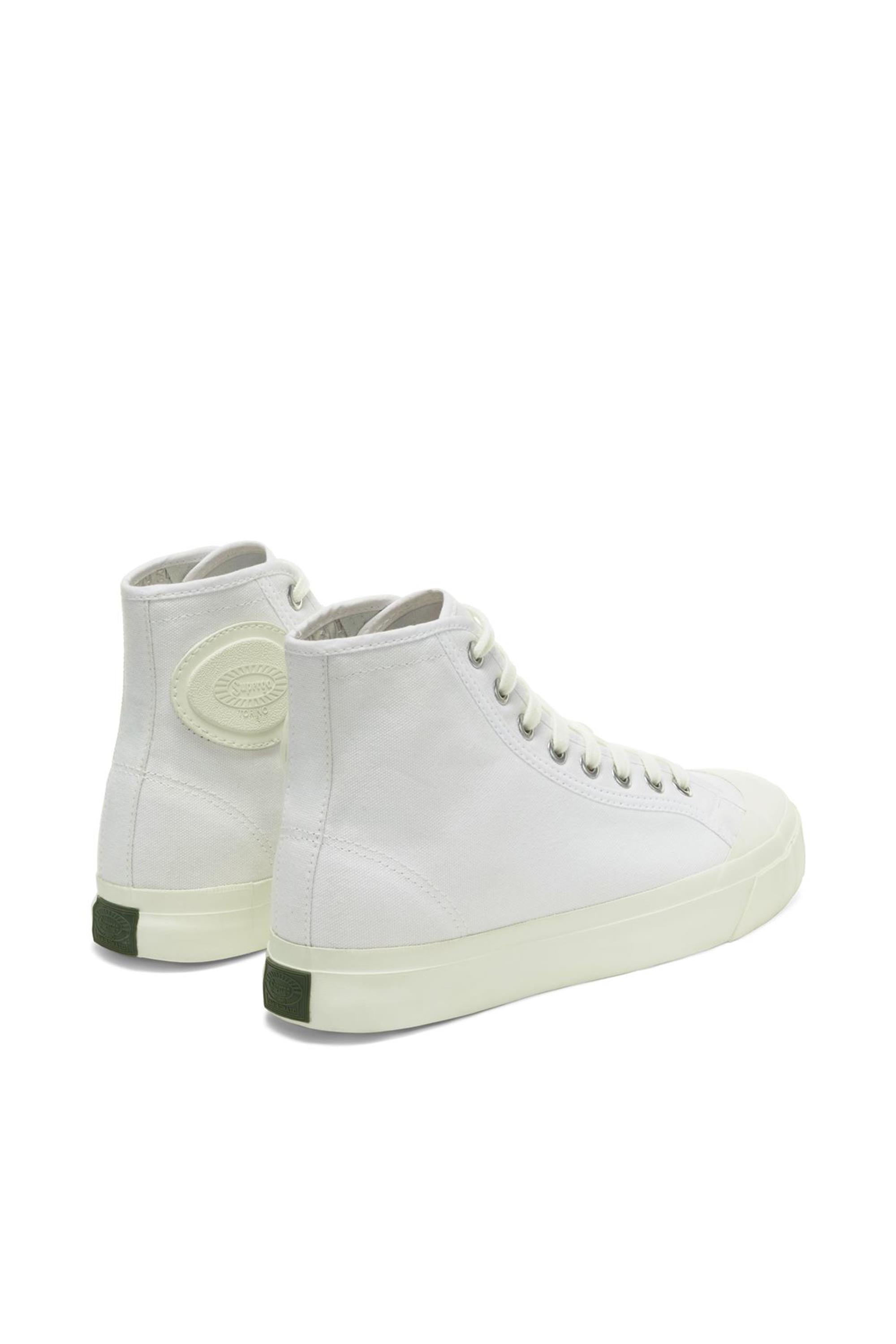 The Superga Campinato Basket by Superga is a pair of white high-top canvas sneakers with white laces, off-white vulcanized natural rubber soles, a green heel accent, and an embossed circular logo near the ankle. Inspired by 70s basketball style.