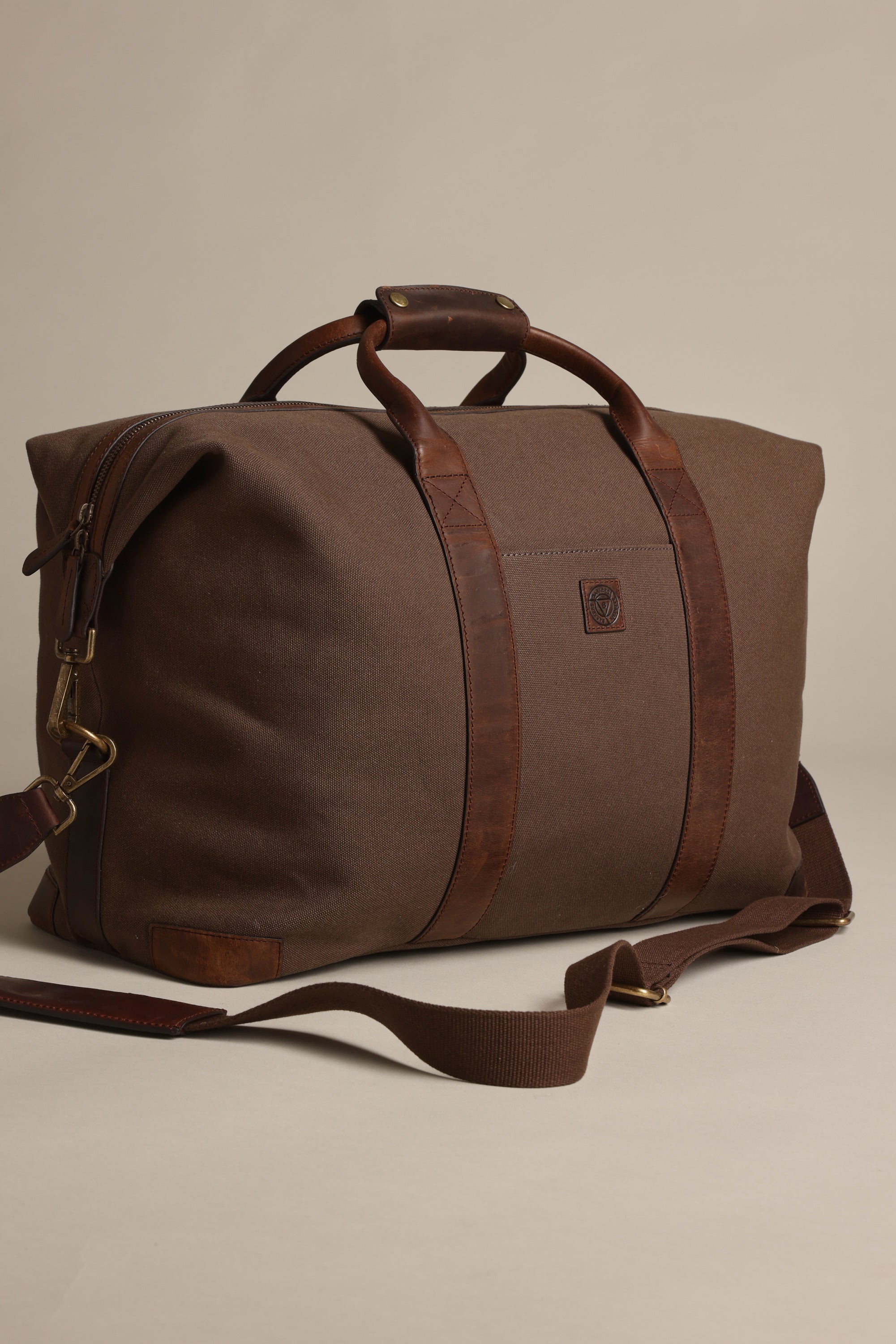 The Barkers Newman Canvas Weekender is a brown travel bag with leather handles and a detachable shoulder strap, displayed on a plain beige background.