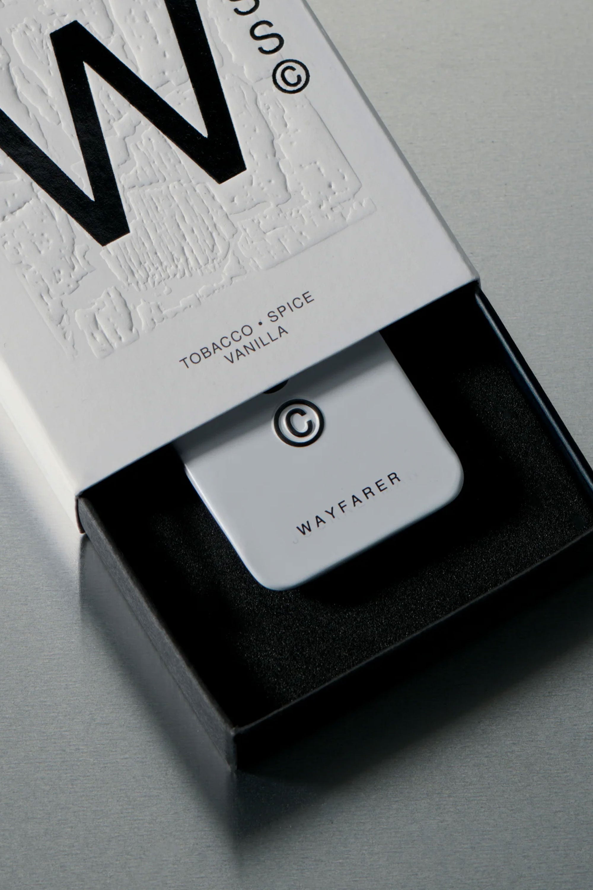 A white rectangular Solid State - Wayfarer device with a large W sits in a black foam-lined box; the packaging highlights TOBACCO • SPICE VANILLA, indicating a wax-based solid cologne by Solid State.